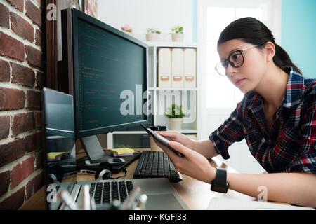 elegant attractive female programmer using mobile pad computer working and looking at laptop to think new website design idea. Stock Photo