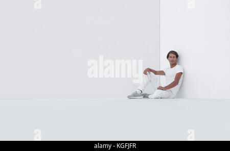 sad young man sitting beside a white wall Stock Photo