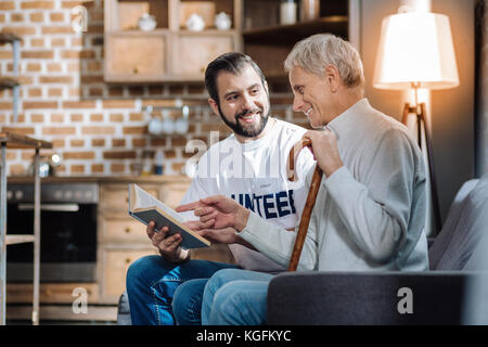 Happy pensioner discussing an interesting book with a young volunteer Stock Photo