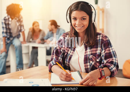 Smiling young woman wearing headphones and making notes Stock Photo