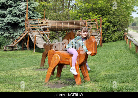 little girl riding wooden horse on playground Stock Photo