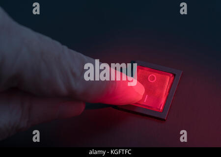Finger hovering over illuminated red electrical switch - potential metaphor for 'stopping', switching, on-off, stopping & starting things in general Stock Photo