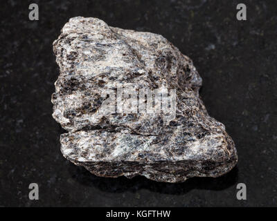 macro shooting of natural mineral rock specimen - rough quartz-biotite schist stone on dark granite background Stock Photo