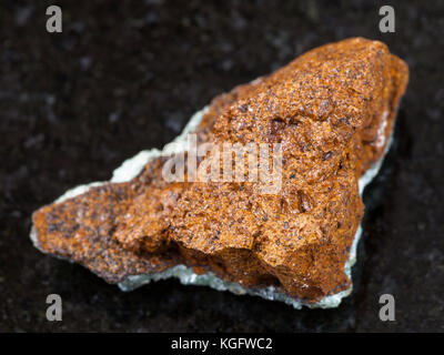 macro shooting of natural mineral rock specimen - raw bog iron ore ( limonite) stone on dark granite background from Taman Peninsula, Russia Stock Photo