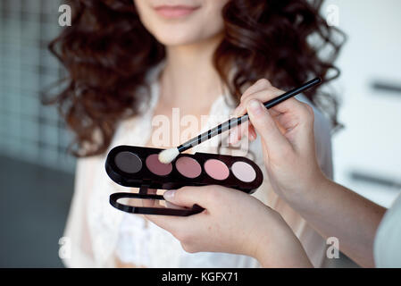 Makeup artist applies eye shadow. Perfect smooth skin.Applying makeup. Application of shadows on the model's eyes. Stock Photo
