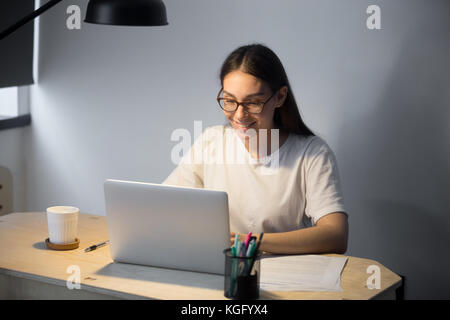 Young adult woman working on laptop computer late at night. Girl doing video chat job interview for position in remote town in evening at workplace de Stock Photo