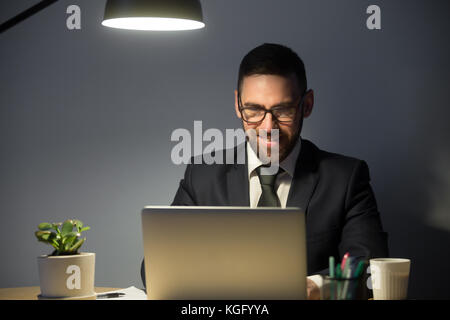 Young adult man in glasses working on laptop computer late at night. Man doing video chat job interview for position in remote town in evening at work Stock Photo