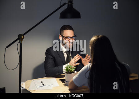 Two businesspeople planning corporate event after successfully finishing project in late evening meeting. Excited bearded man in glasses speaking with Stock Photo