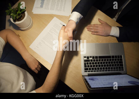 Handshake top close up view. Two businesspeople shake hands to seal a deal, laptop computer with rising stats on the desk. Human resources manager pro Stock Photo