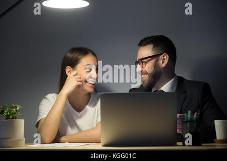 Two corporate employee having good time in late evening meeting. Happy businesspeople smiling after seeing last project successful results on laptop c Stock Photo