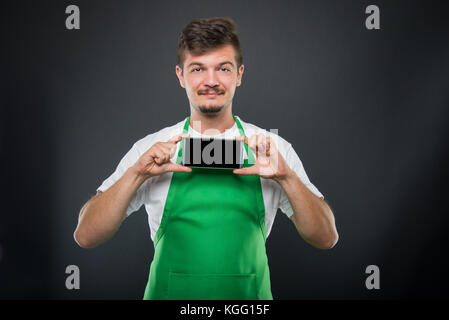 Portrait supermarket employer holding smartphone and smiling on black background Stock Photo