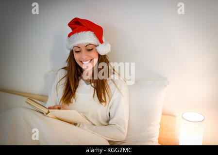 Beautiful smiling girl in white cozy bed reading a book waiting for Christmas. Stock Photo