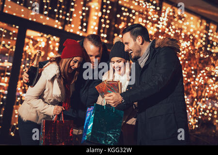 Happy beautiful young couples holding gifts they bought, while standing in mall and checking their shopping bags. Stock Photo