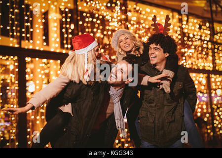 Cheerful happy friends having fun in city mall in Christmas night, with bright shop window in background. Stock Photo