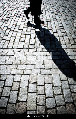 legs of a person projecting long and strong shadow on the street Stock Photo
