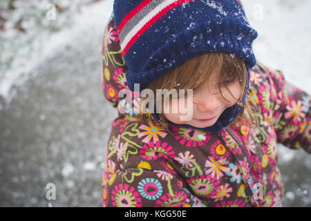 A toddler stands outside wearing winter clothes with snow around her. Stock Photo