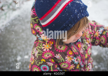 A toddler stands outside wearing winter clothes with snow around her. Stock Photo