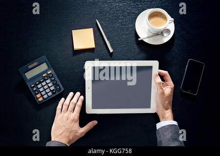 business man hands on a black wooden table with tablet, phone, cup of coffee, calculator, sticky note papers and pen in a office, view from above Stock Photo