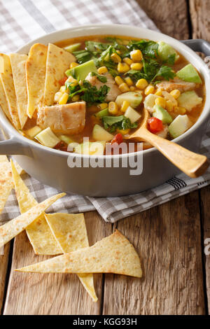 Mexican food: tortilla soup with chicken, tomatoes, avocado and corn close-up in a saucepan on a table. vertical Stock Photo