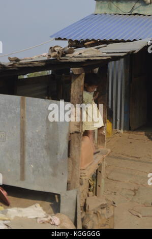 little girl standing in a metal shack staring at the ground while holding on to wooden pillar. Nepal, Bacheck, destroyed during earthquake. No school. Stock Photo