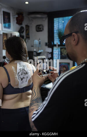 A Tattoo Artist at Work,A tattoo artist inks a designed onto the back of a local girl in his studio in Leeds. Stock Photo