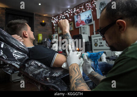 A Tattoo Artist at Work,A tattoo artist inks a designed onto the back of a local girl in his studio in Leeds. Stock Photo