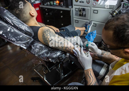 A Tattoo Artist at Work,A tattoo artist inks a designed onto the back of a local girl in his studio in Leeds. Stock Photo