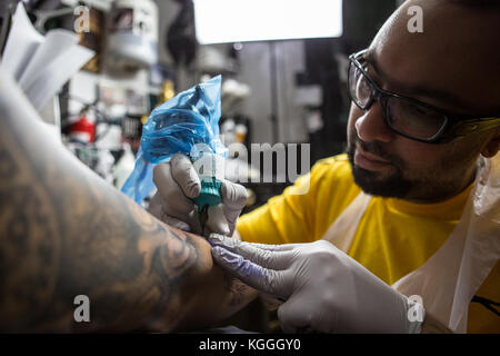 A Tattoo Artist at Work,A tattoo artist inks a designed onto the back of a local girl in his studio in Leeds. Stock Photo