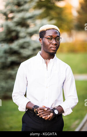 Young handsome afro american man with blonde hair walking in the sunny city streets. Stock Photo