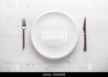 Top of view empty plate with fork and knife on white concrete background. Stock Photo