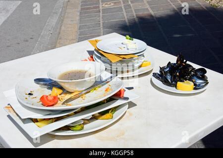 Dirty plates stacked on a restaurant table ready to be washed along the waterfront, Marsaxlokk, Malta, Europe. Stock Photo