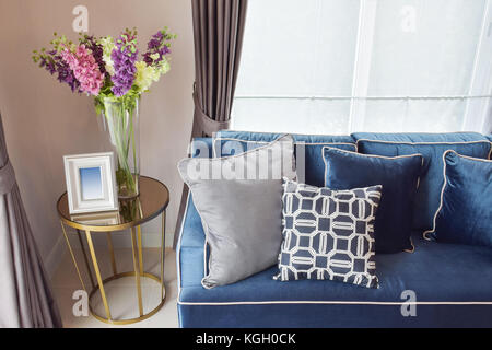 Navy blue modern classic sofa and retro, gray and blue pillows with a lovely orchid vase on side table in living corner Stock Photo