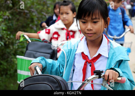 BINH DINH, VIET NAM- NOV 3, 2017:Group of Vietnamese children coming home from school by bicycle, crowd Asian little girl ride cycle on country road,  Stock Photo