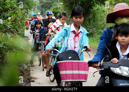 BINH DINH, VIET NAM- NOV 3, 2017:Group of Vietnamese children coming home from school by bicycle, crowd Asian little girl ride cycle on country road,  Stock Photo