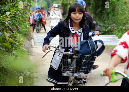 BINH DINH, VIET NAM- NOV 3, 2017:Group of Vietnamese children coming home from school by bicycle, crowd Asian little girl ride cycle on country road,  Stock Photo