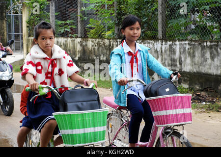 BINH DINH, VIET NAM- NOV 3, 2017:Group of Vietnamese children coming home from school by bicycle, crowd Asian little girl ride cycle on country road,  Stock Photo