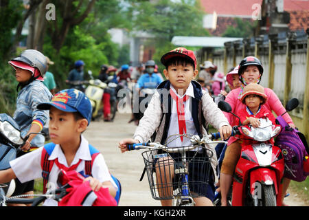 BINH DINH, VIET NAM- NOV 3, 2017:Group of Asian children coming home from school by bicycle, crowd Vietnamese pupil ride bike on country road, Vietnam Stock Photo