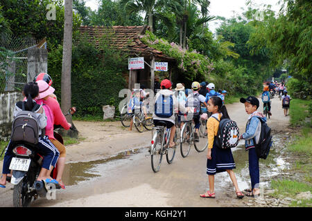 BINH DINH, VIET NAM- NOV 3, 2017:Group of Asian children coming home from school by bicycle, crowd Vietnamese pupil ride bike on country road, Vietnam Stock Photo