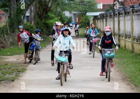 BINH DINH, VIET NAM- NOV 3, 2017:Group of Asian children coming home from school by bicycle, crowd Vietnamese pupil ride bike on country road, Vietnam Stock Photo