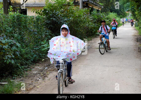 BINH DINH, VIET NAM- NOV 3, 2017:Group of Asian children coming home from school by bicycle, crowd Vietnamese pupil ride bike on country road, Vietnam Stock Photo