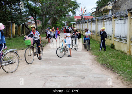 BINH DINH, VIET NAM- NOV 3, 2017:Group of Asian children coming home from school by bicycle, crowd Vietnamese pupil ride bike on country road, Vietnam Stock Photo