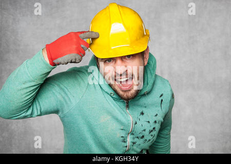 A mad disgruntled worker peeking in a protective helmet Stock Photo