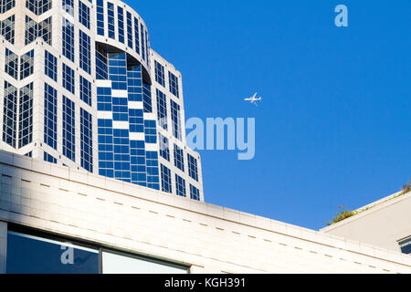 Street view of U.S. Bank building in Seattle, Washington with jet airplane flying over in a clear, blue sky. Stock Photo