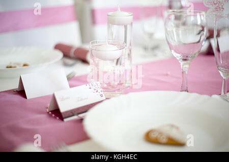 Pink and white wedding table with small round white tea candle in a clear glass, pink runner, empty wine glasses, white plate Stock Photo