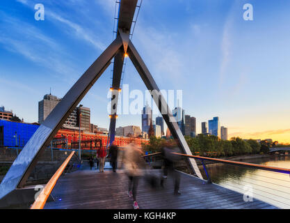 Blurred walking people crossing Yarra river on foot bridge connecting Melbourne CBD with South Bank at early morning rushing to offices. Stock Photo