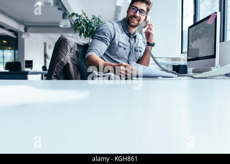 Businessman sitting in office and talking on telephone. Young man using phone at his workplace. Stock Photo