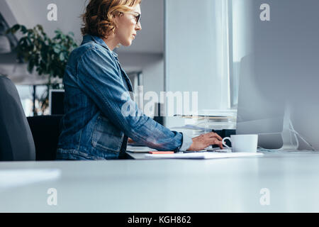 Side view of young businesswoman working in office. Female designer sitting and using laptop. Stock Photo
