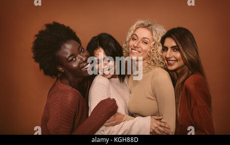 Group of cheerful young women standing together on brown background. Multi ethnic female friends in studio. Stock Photo