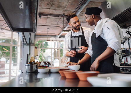 Two male cooks preparing food on restaurant kitchen. Chefs talking while cooking food in commercial kitchen. Stock Photo