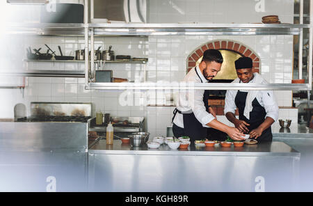 Professional chefs working in commercial kitchen preparing food dish together. Chefs cooking food at commercial kitchen. Stock Photo